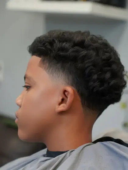 A curly top with a skin fade, in profile, cut by Leandro Herrera